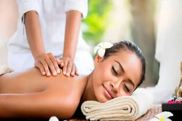 Mujer disfrutando un masaje relajante en un ritual spa. Una flor adorna su cabello mientras manos expertas alivian la tensión de su espalda.