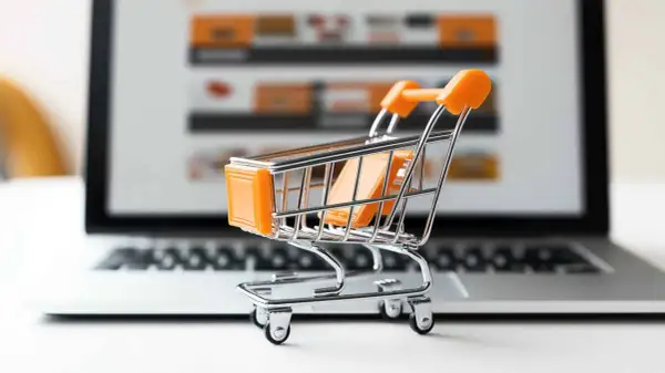 Miniaturowy wózek na zakupy przed ekranem laptopa symbolizuje najpopularniejsze sklepy internetowe i wygodne zakupy online.