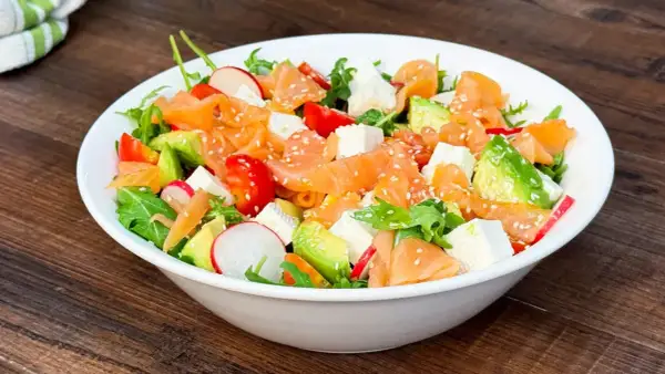 Insalata fresca con salmone affumicato, avocado, pomodorini, ravanelli e cubetti di formaggio, cosparsa di semi di sesamo.