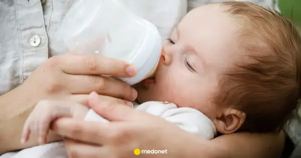 Dziecko pije mleko modyfikowane z butelki. Mama karmi maluszka, który spokojnie zasypia.