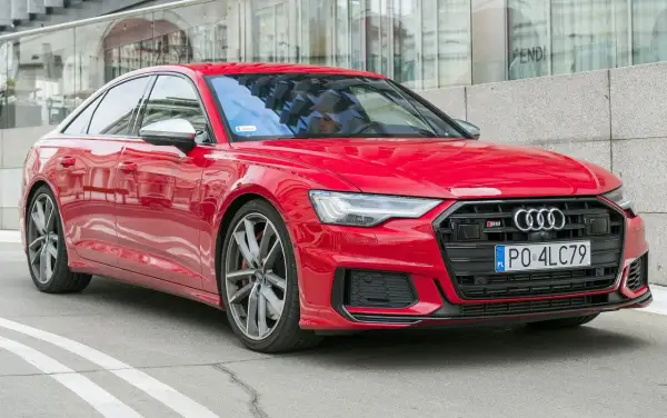 Czerwone Audi S6 C8 z polskimi tablicami rejestracyjnymi, zaparkowane przed nowoczesnym budynkiem z lustrzaną fasadą.
