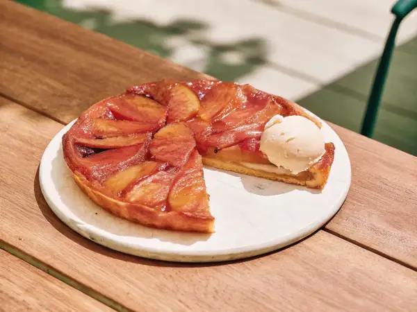 Tarte Tatin aux pommes caramélisées avec une boule de glace à la vanille sur une assiette blanche.