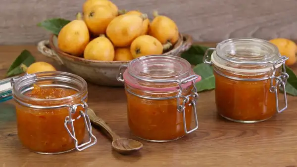 Tre barattoli di marmellata di nespole fatti in casa, con nespole fresche in una ciotola sullo sfondo.