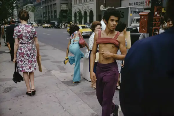Ulica Nowego Jorku uchwycona przez Joel Meyerowitz. Mężczyzna w bordowym topie i fioletowych spodniach, obok kobiety w kwiecistej sukience.