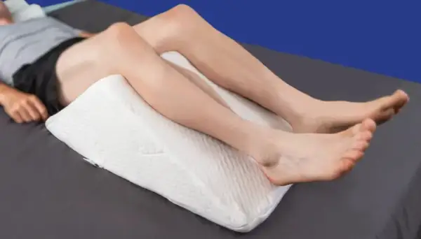 A person is resting with a white wedge pillow under their knees, providing comfort for sleeping with pillow under knees.