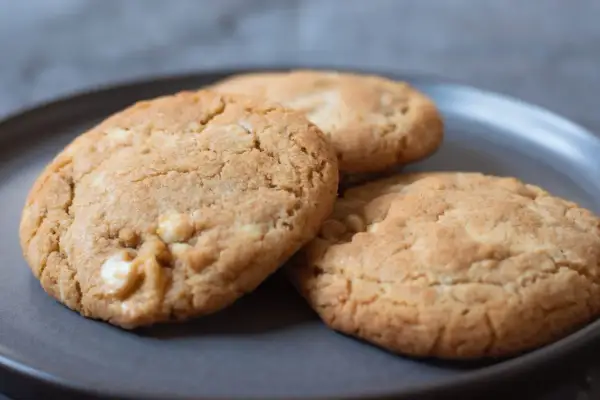 Tre gyllene white chocolate chip cookies på en mörkgrå tallrik, redo att avnjutas.