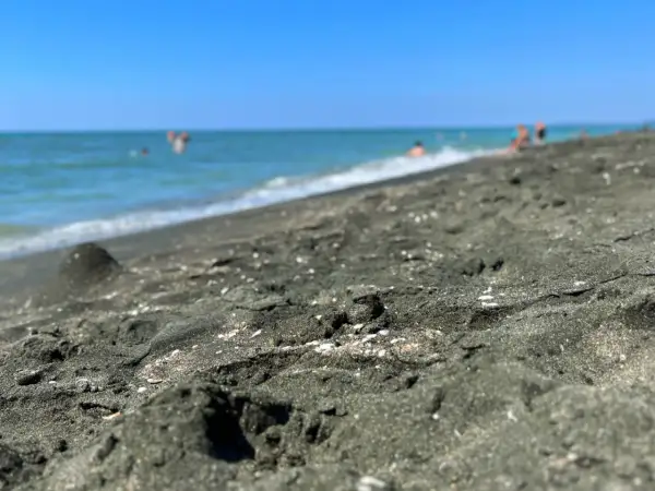 Ciemny piasek na plaży w Ureki, Gruzja. W tle widać turkusowe morze i kąpiących się ludzi.