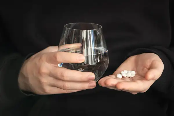 Dwie dłonie trzymają szklankę wody i garść białych tabletek. Zastanawiasz się, czy można pić alkohol po Ibupromie?