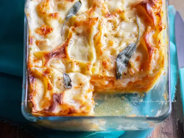 Lasagne con zucca dorate e filanti, guarnite con foglie di salvia, in una teglia di vetro.