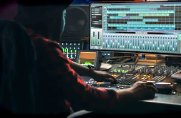 Persona trabajando en una mesa de mezclas, con una pantalla mostrando pistas de audio. Ideal para masterización online gratis.