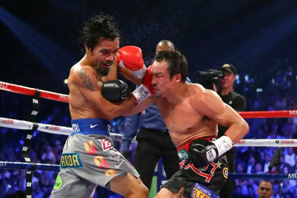 Manny Pacquiao lands a punch on Juan Manuel Marquez during their intense boxing match. Sweat flies as the crowd roars.