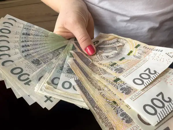 Dłoń trzyma wachlarz polskich banknotów 100 i 200 zł. To może być nagroda jubileuszowa nauczycieli.