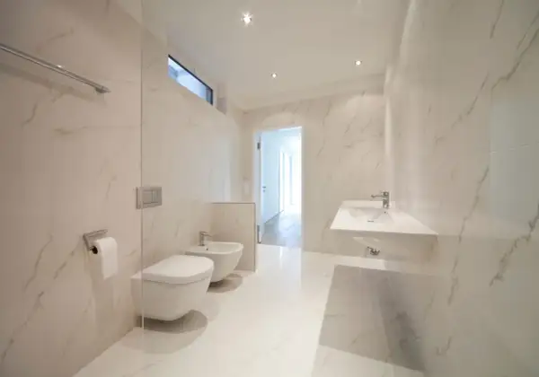 Bagno moderno con bidet e WC sospesi, lavabo a mensola e finiture in marmo. L'altezza scarico bidet è ottimale per un uso confortevole.