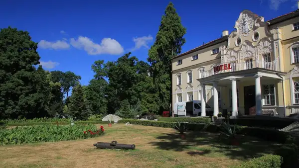Pałac w Witaszycach, dawniej hotel, otoczony zielenią. Na trawniku leży zabytkowa armata.