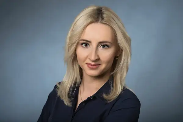Portret uśmiechniętej blondynki w granatowej koszuli na niebieskim tle.