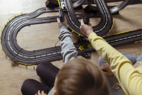Dwie osoby sterują samochodzikami na torze wyścigowym, trzymając kontrolery.