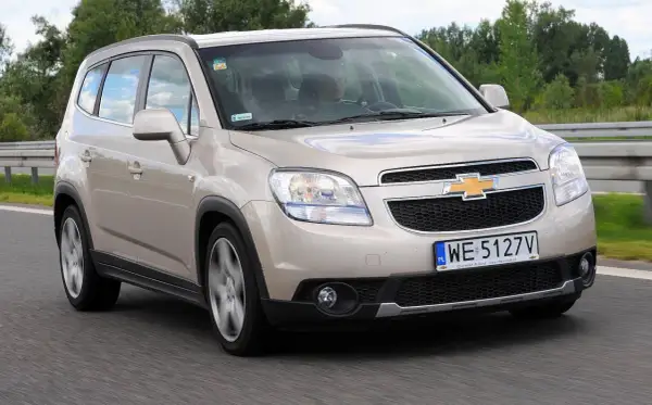 Złoty Chevrolet Orlando 1.8 benzyna na drodze. Rodzinny minivan w ruchu, z widocznym kierowcą.