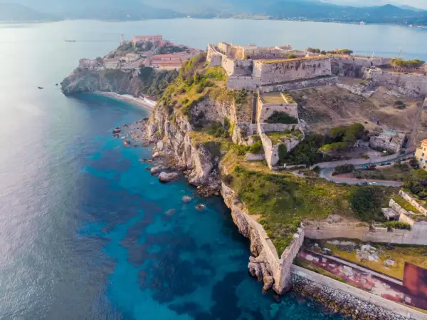 Fortificazioni storiche su una scogliera a picco sul mare turchese, un gioiello delle città della Toscana.