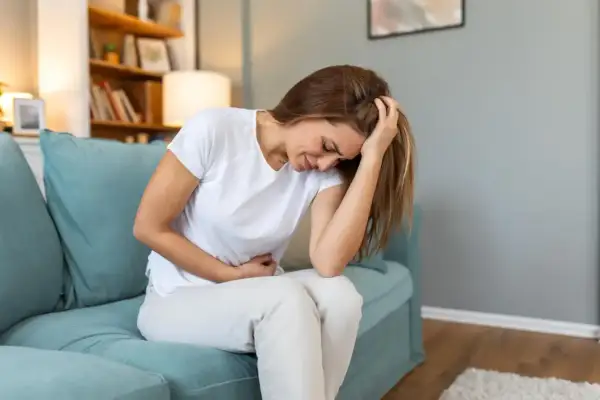 Femme assise sur un canapé bleu, se tenant le ventre et la tête, visiblement souffrante. Elle pourrait exprimer la douleur liée à l'endométriose profonde.