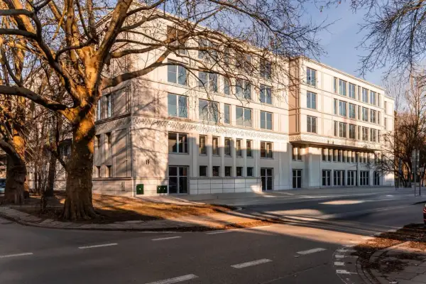 Nowoczesny budynek mieszkalny z dużymi oknami i drzewami w pobliżu, w słoneczny dzień.