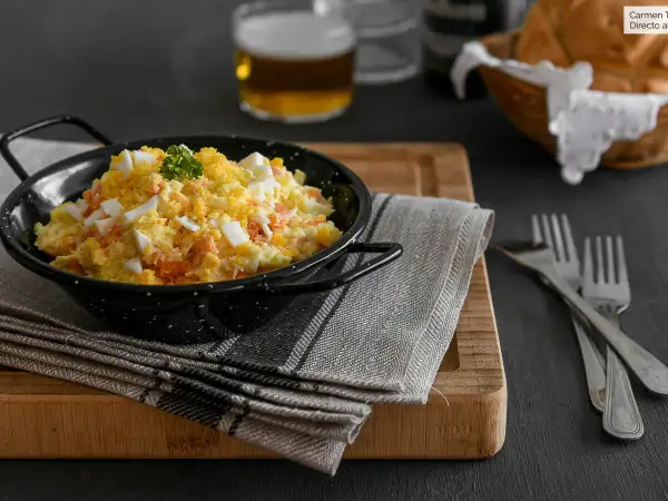 Una deliciosa ensalada rusa, cremosa y con trozos de huevo duro y zanahoria, servida en un cuenco negro.