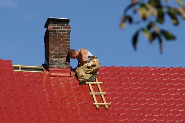 Handwerker dichtet den Schornstein am roten Ziegeldach ab.