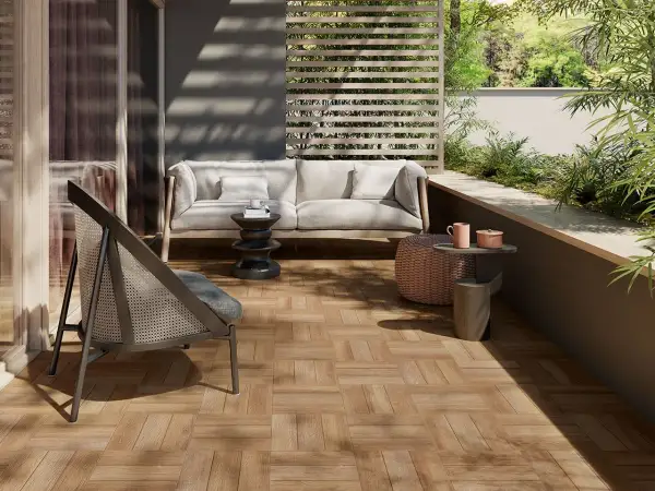 Terrazzo con pavimenti in gres porcellanato effetto legno, arredato con divano, poltrona e tavolini, immerso nel verde.