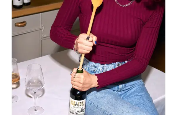 Korken ohne Korkenzieher: Eine Person versucht, eine Weinflasche mit einem Holzlöffel zu öffnen.