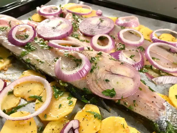 Lavarello in padella pronto per la cottura, con patate affettate, cipolla rossa a rondelle e prezzemolo fresco.