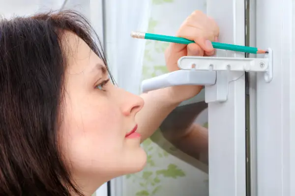 Une femme ajuste une vis de réglage sur une fenêtre PVC avec un crayon.
