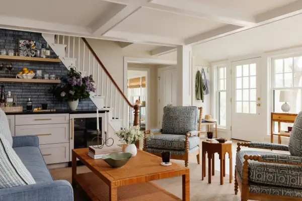 A living room with a traditional style, featuring blue patterned armchairs, a rattan coffee table, and a bar area with blue tiled backsplash.