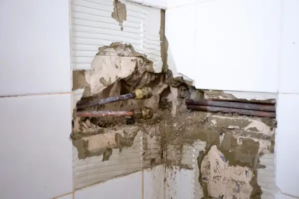 Beschädigte Wand mit freiliegenden Kupferrohren und Armaturen. Ein **Rohrbruch was tun**? Sofort Wasser abstellen und Fachmann rufen.