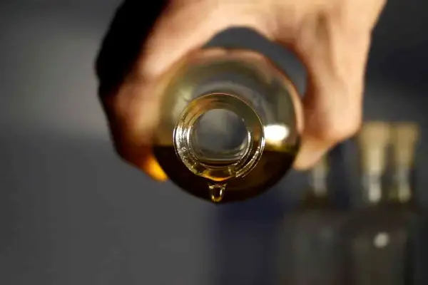 Une goutte d'huile dorée tombe d'une bouteille, parfait pour votre huile cheveux maison.
