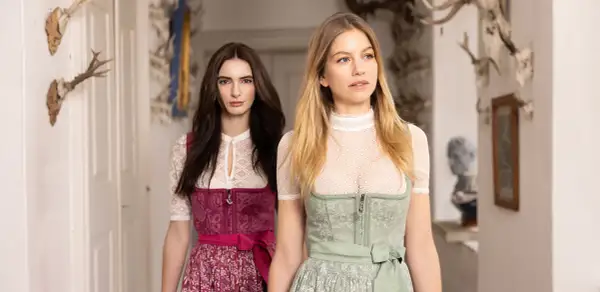 Zwei Frauen in Tracht, eine mit dunkelbraunem, die andere mit blondem Haar, präsentieren elegante dirndlschürzen lang.