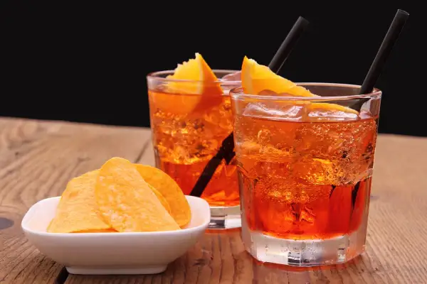 Dwa orzeźwiające drinki z pomarańczą i słomkami, obok miseczka chipsów. Idealne aperitif przykłady na letnie popołudnie.