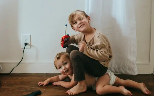 Twee broertjes spelen op de grond. De oudste zit op de rug van de jongste en houdt een speelgoedwalkietalkie vast. Dit is waarom maken broers en zussen ruzie.