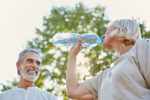 Un couple profite du soleil, la femme boit de l'eau pour une hydratation optimale, l'homme sourit.