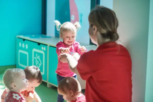 Wesoła dziewczynka z kitkami, w różowej bluzce, pokazuje coś dorosłej osobie. Widać też inne dzieci. To pokazuje, jak różny jest temperament co to.