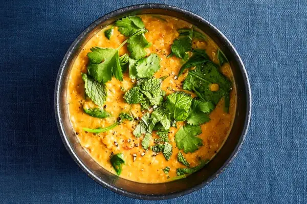 Ein dampfender Linsen-Curry in einer Schüssel, garniert mit frischem Koriander und Minze.