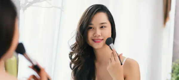 Une jeune femme applique du maquillage pour peau grasse avec un pinceau.