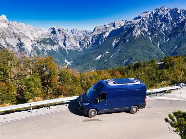 Blauer Campervan auf Bergstraße in Albanien. Perfektes Wetter im August für eine Reise durch die beeindruckende Berglandschaft.