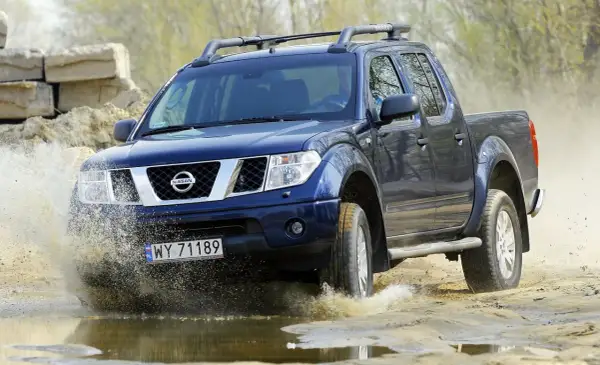 Niebieski Nissan Navara pokonuje wodną przeszkodę, rozpryskując błoto.