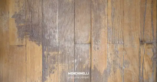 Parquet rovinato dall'acqua, con doghe in legno che mostrano macchie scure e usura, testimoni di un passato umido.