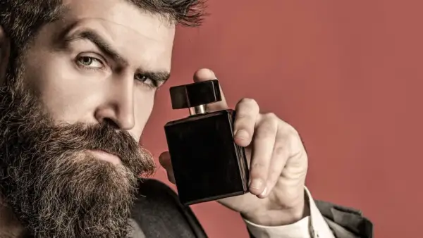 Mężczyzna z brodą trzyma czarną buteleczkę perfum, zastanawiając się, gdzie psikać perfumy, by podkreślić swój styl.