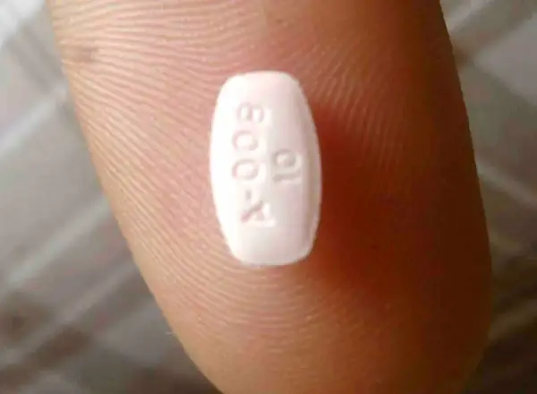 Biała tabletka z oznaczeniem "A-009 10" na palcu. Może to być lek, np. Abilify, pomagający w leczeniu schizofrenii.