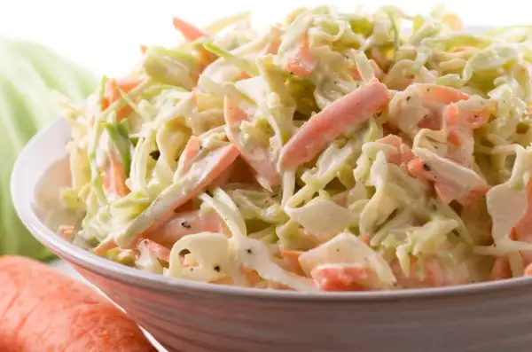 Miseczka surówki coleslaw z poszatkowanej kapusty i marchewki w kremowym sosie.