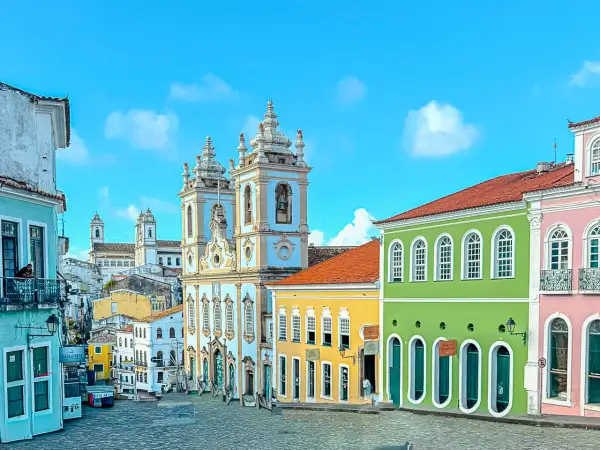 Calles empedradas y coloridas casas coloniales bajo un cielo azul en **Bahía, Brasil**. Una iglesia barroca domina el paisaje.