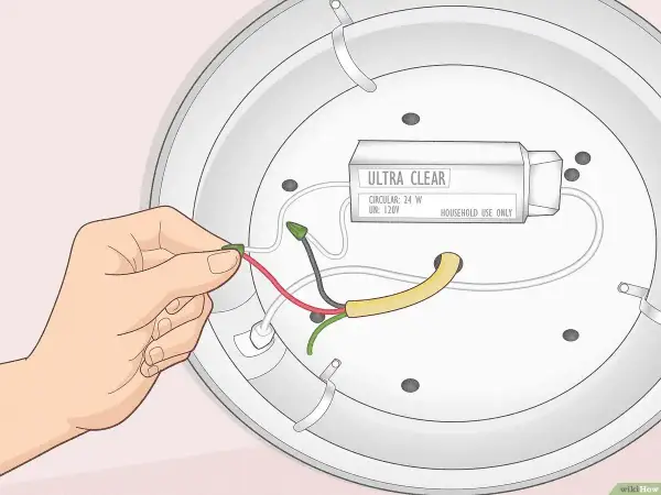 Main d'une personne effectuant le branchement d'un éclairage, connectant un fil rouge à un connecteur vert.