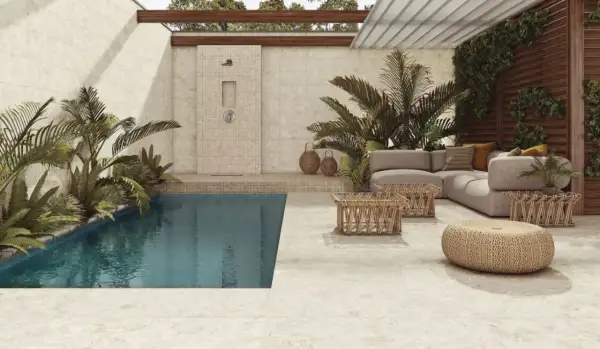 Piscina y zona lounge con sofás y mesas bajas, ducha exterior y plantas exuberantes. El suelo y las paredes lucen un elegante microcemento exterior.