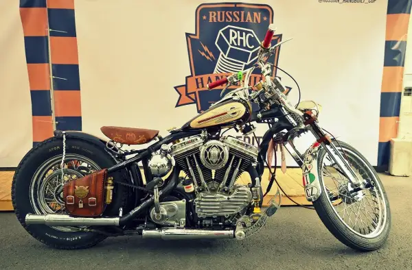 Customowy motocykl z chromowanymi elementami, skórzanym siedzeniem i sakwą, na tle baneru Russian RHC.